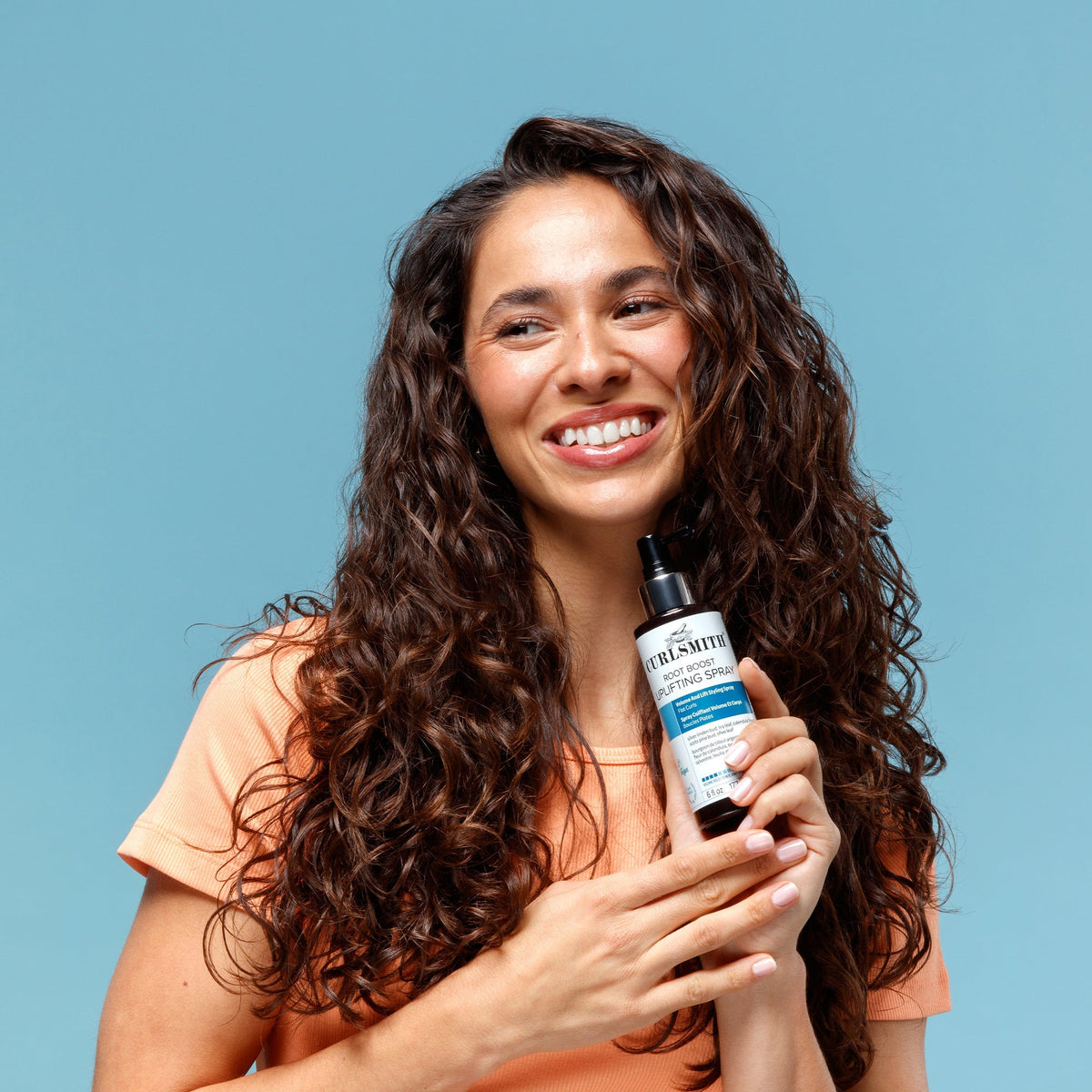 Woman holding a bottle of Fruithive hair product against a blue background