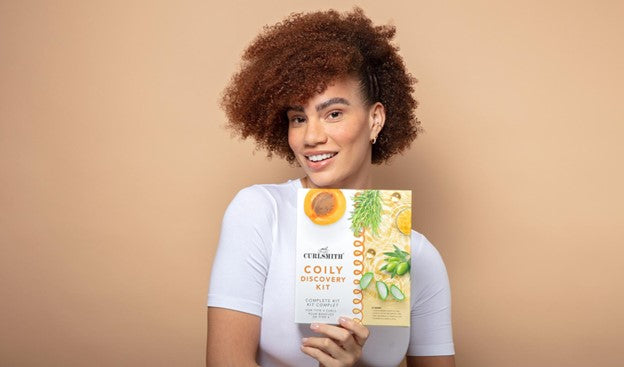 woman with coily hair holds up the curlsmith coily discovery hair kit product