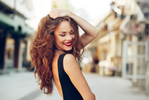 A smiling person with wavy red hair and a black dress