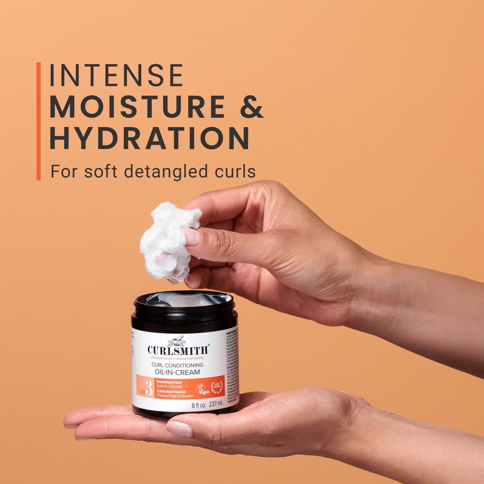 Person holding a jar of Curlsmith product with cream on fingers against an orange background