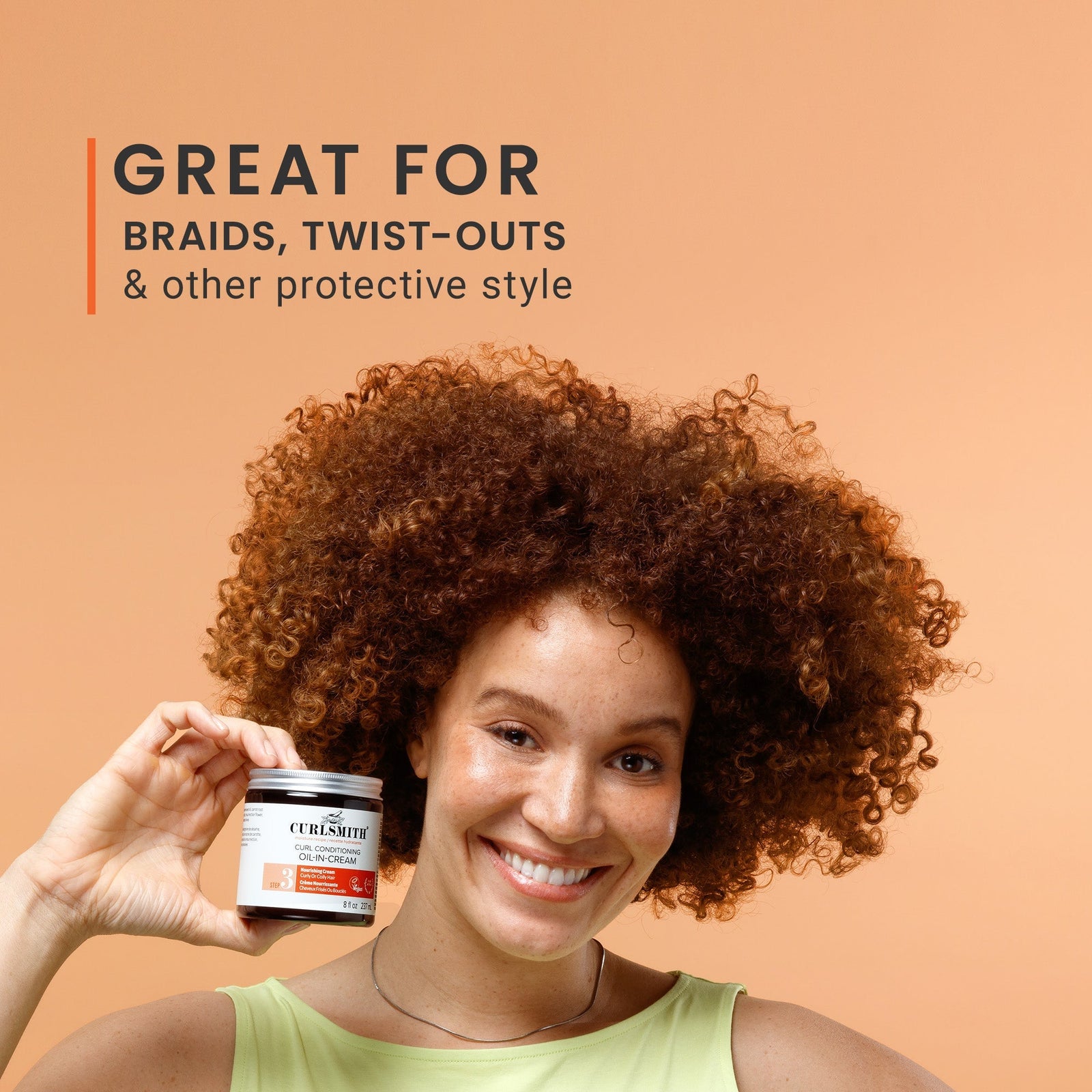 Woman with curly hair holding a jar of hair product against an orange background