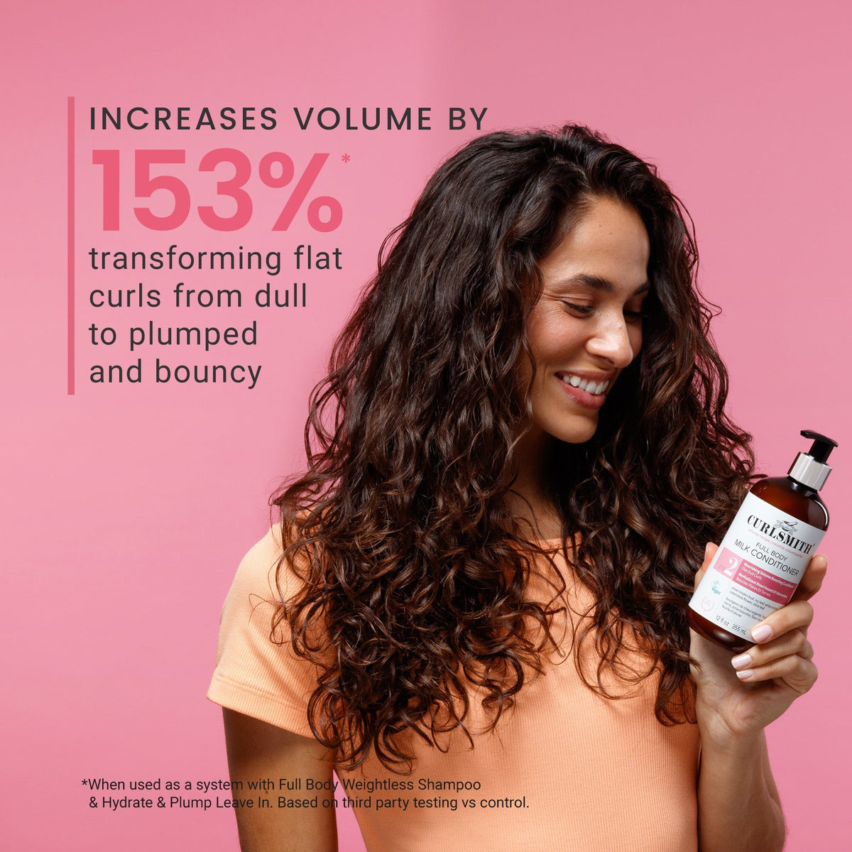 Woman with long, wavy hair holding a bottle of shampoo against a pink background