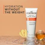 Tube of Curlsmith weightless air dry cream on a wooden surface with bananas and a glass of liquid in the background.